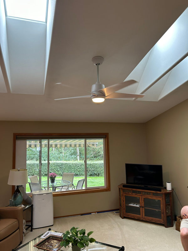 A beautiful living room features a sleek ceiling fan. Skylights let in natural light, while a view of the garden adds a fresh touch. The cozy space is perfect for relaxing.